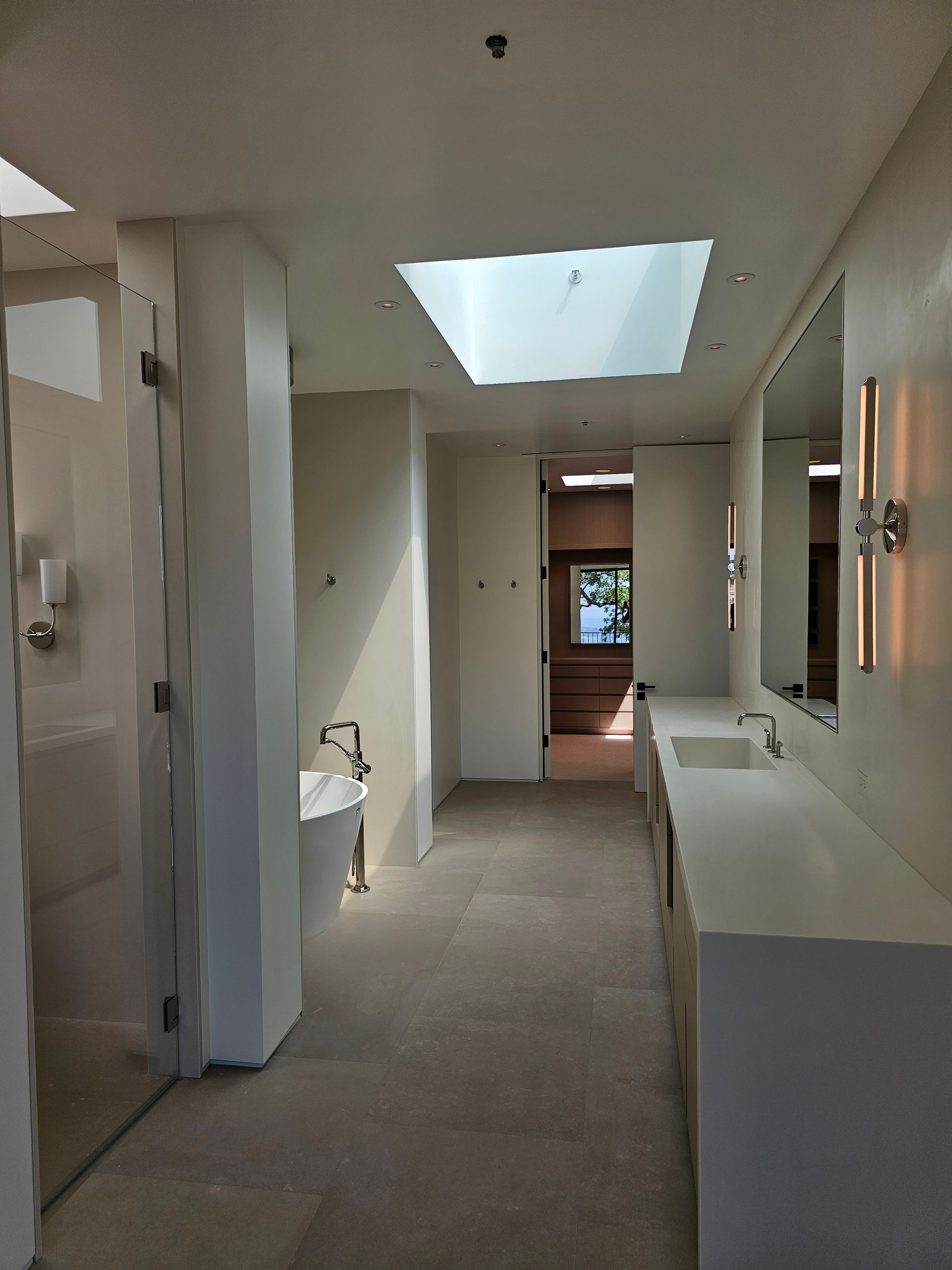 Narrow hallway with skylight, white walls, doors, and a glimpse of stairs at the far end
