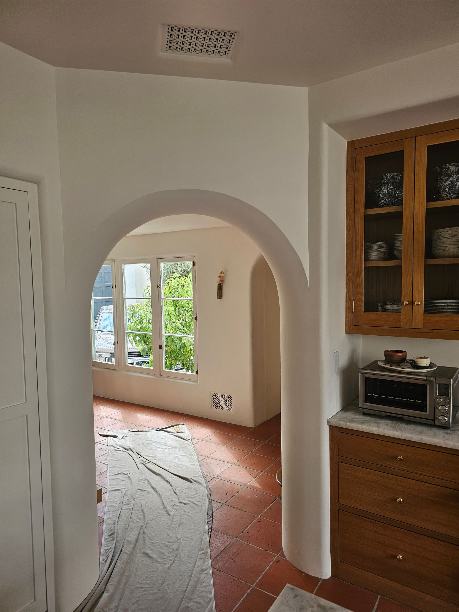 White arched doorway opening to a bright room with windows, tiled floor, and wood kitchen cabinets on the right
