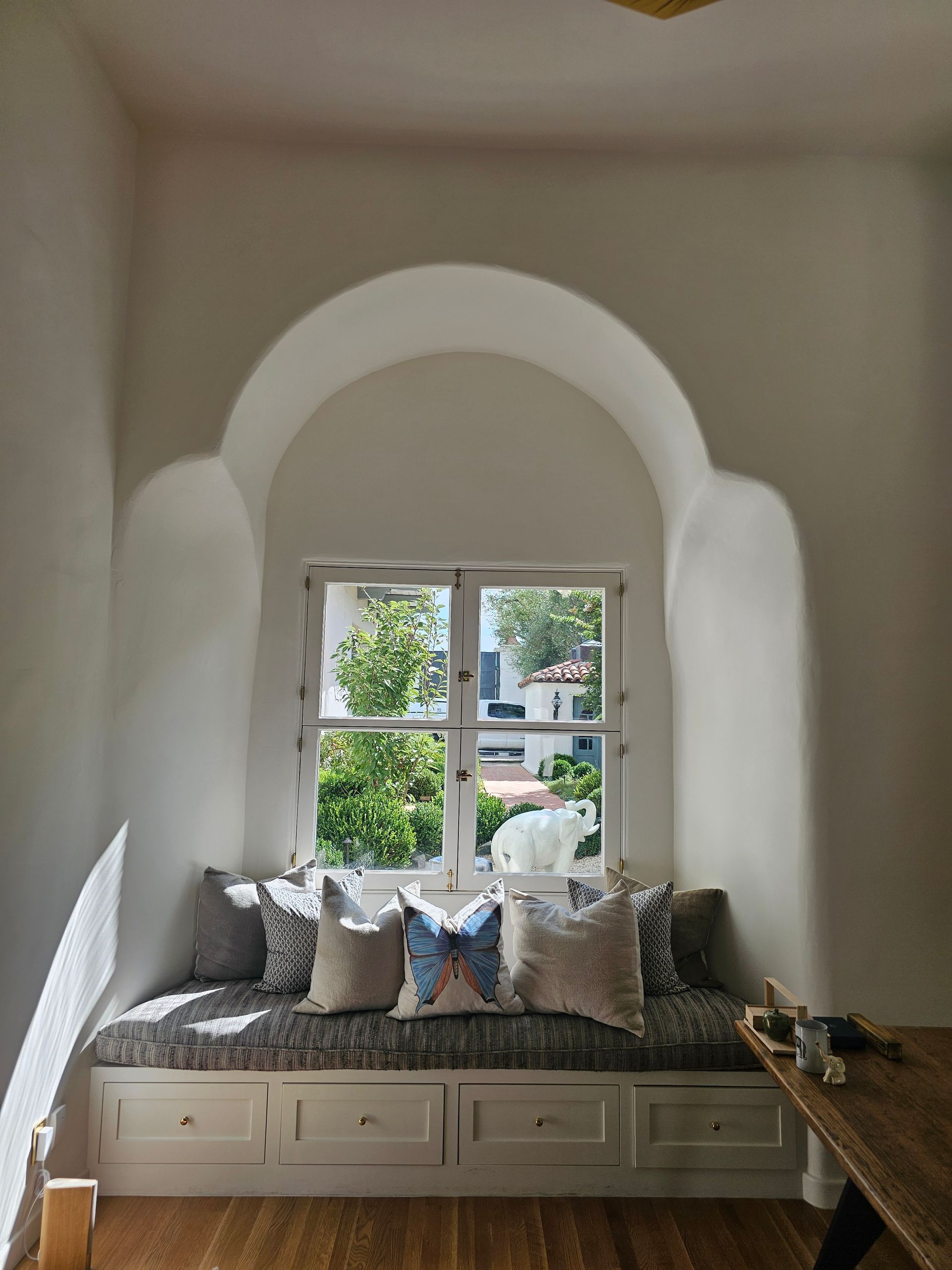 White arched window seat with gray cushions and pillows in a bright nook overlooking greenery