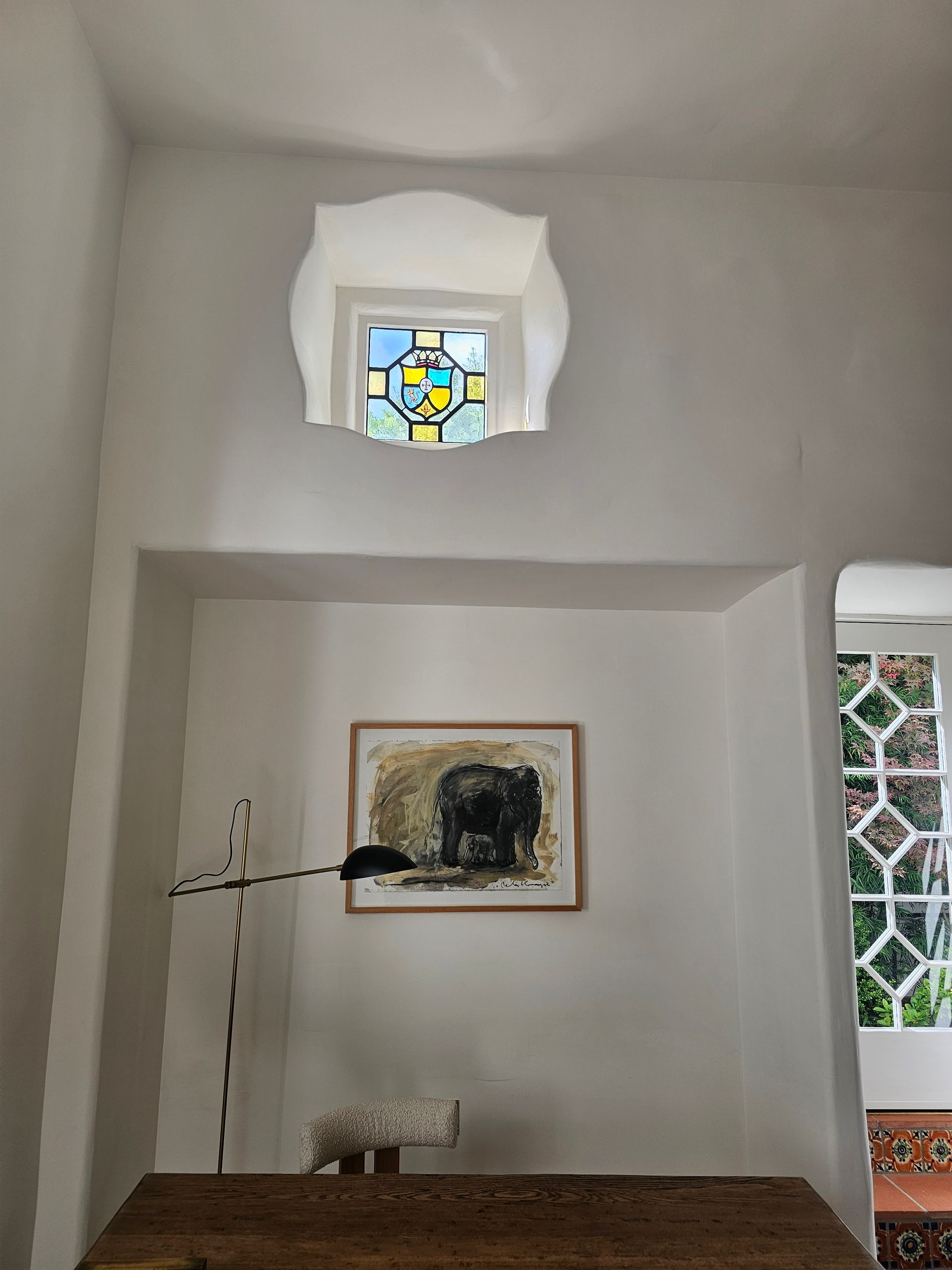 Interior wall alcove with a framed painting, lamp, and narrow stained-glass windows above and to the side