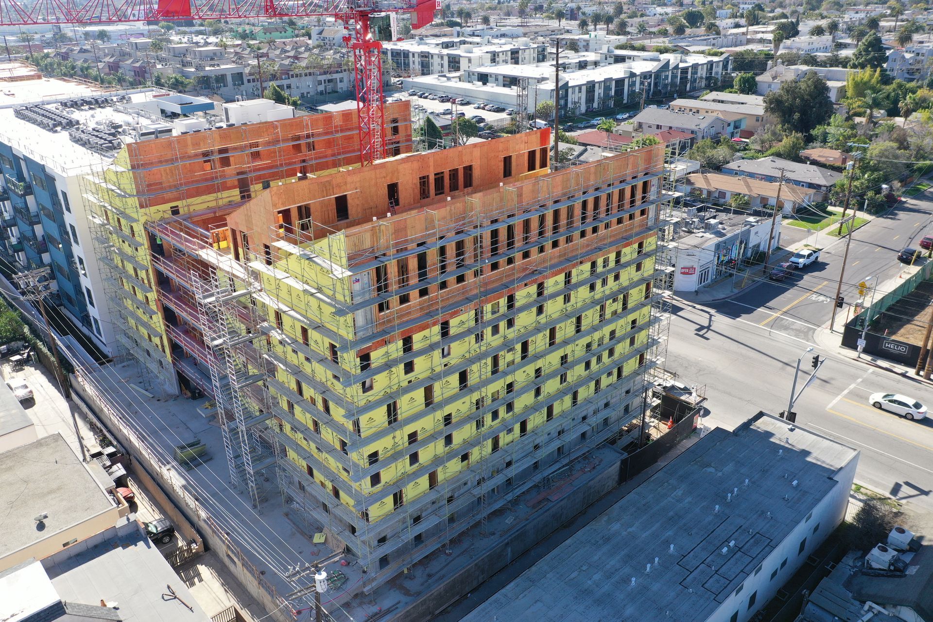 Aerial view of a multistory building under construction with yellow safety netting and a red crane nearby