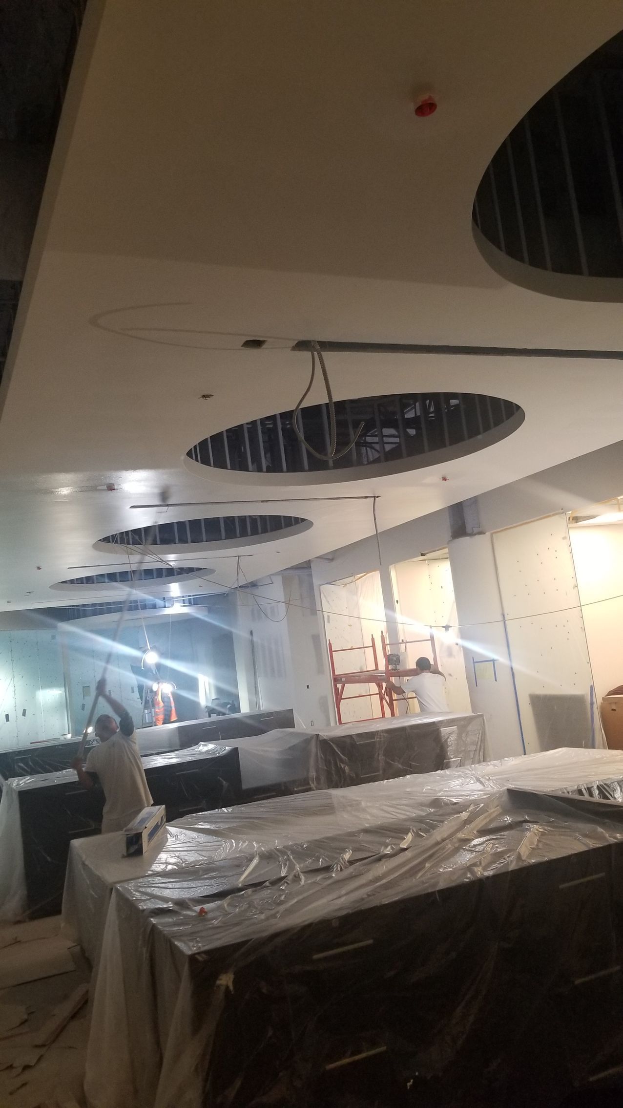 Damaged office interior with exposed ceiling holes, debris, and furniture wrapped in plastic