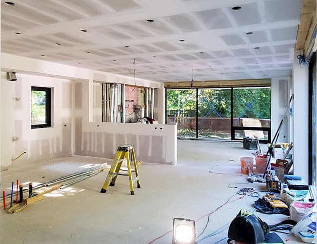 Renovated living room with drywall, tools, ladder, and sliding glass doors to a backyard.
