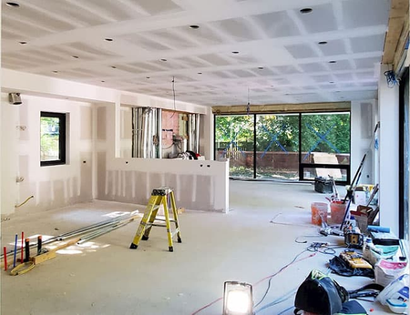 Renovated living room with drywall, tools, ladder, and sliding glass doors to a backyard.
