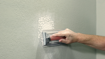 Hand sanding a wall patch with a drywall sanding block next to a textured wall surface