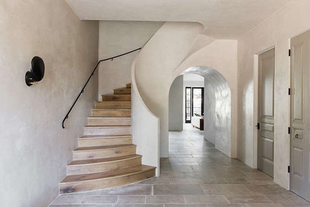 Modern hallway with curved staircase, arched passageways, and light tile flooring