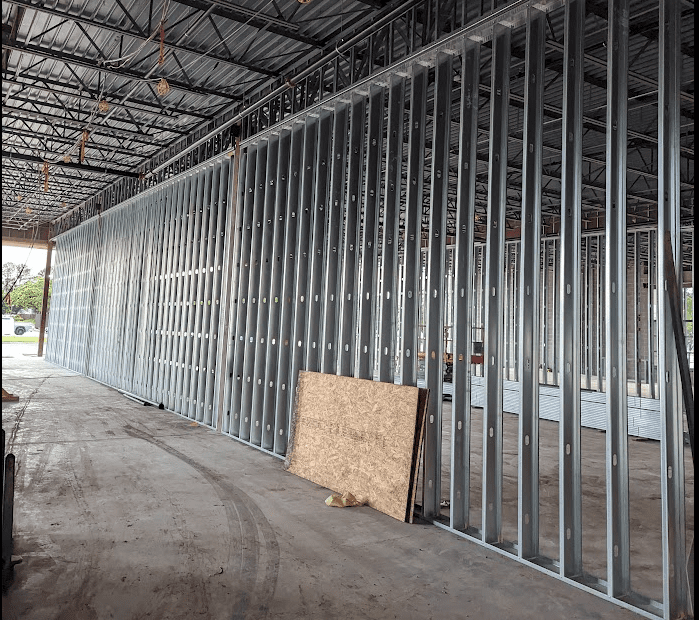 Interior of an unfinished building with steel wall framing and a plywood sheet leaning against it