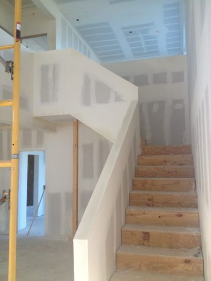 Unfinished interior stairway with wooden steps, white walls, and a doorway on the left.