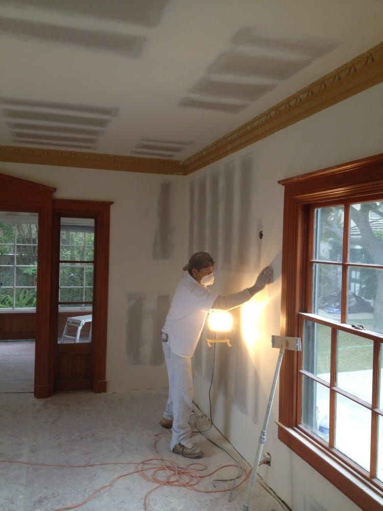 Painter touching up a white wall in a bright room with wood-trimmed windows