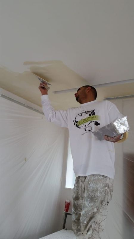 Worker patching a ceiling with a putty knife in a room with white walls and a blue cap