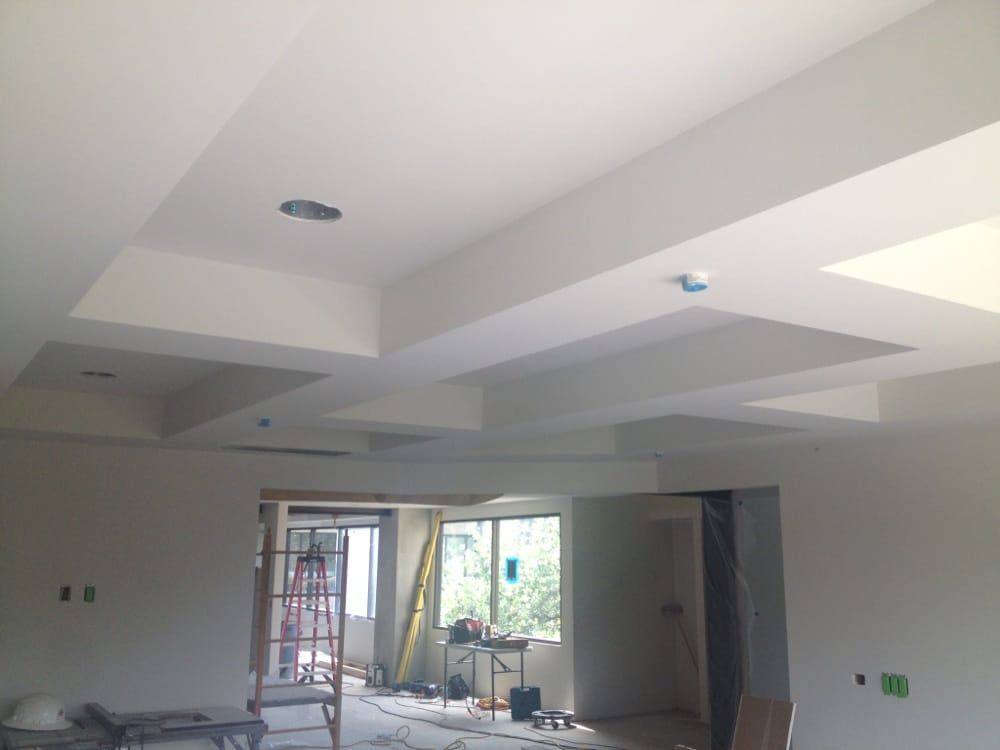 Unfinished room with white ceiling beams, window light, and construction materials on the floor.