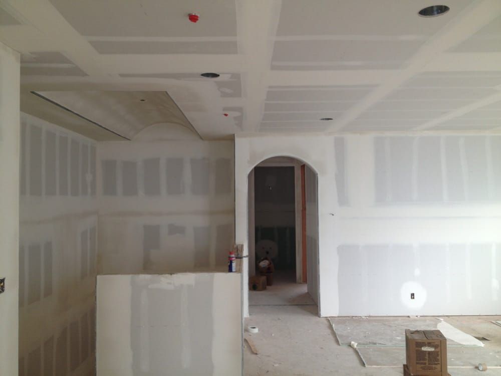Unfinished drywall room with arched doorway, white walls, and construction materials on the floor