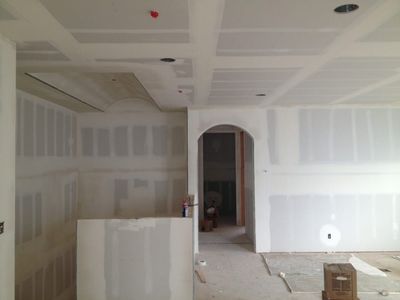 Unfinished drywall room with arched doorway, bare floor, and construction materials.