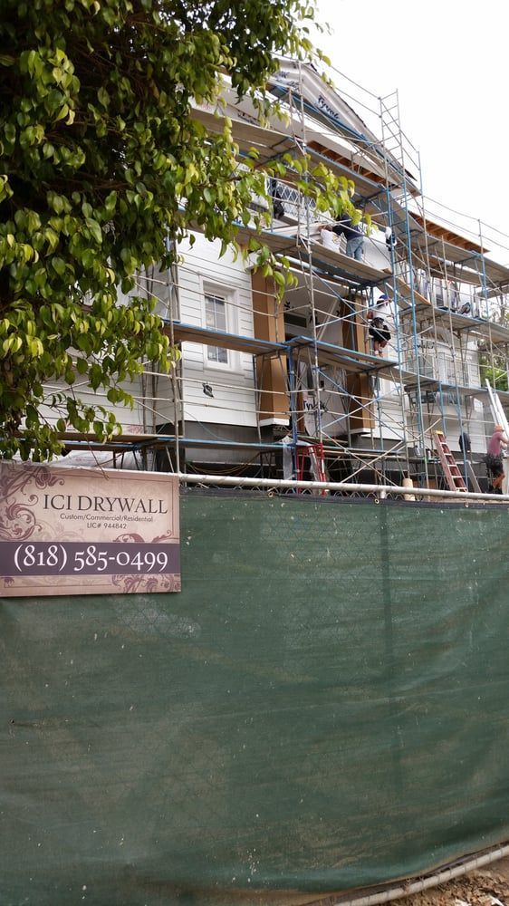 Scaffolding around a white building behind a green construction fence on a street corner.
