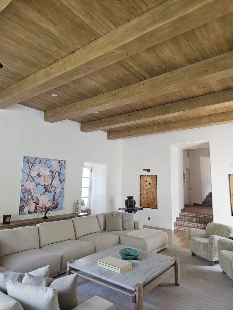 Bright living room with exposed wood ceiling, beige sectional sofa, and coffee table near an open doorway