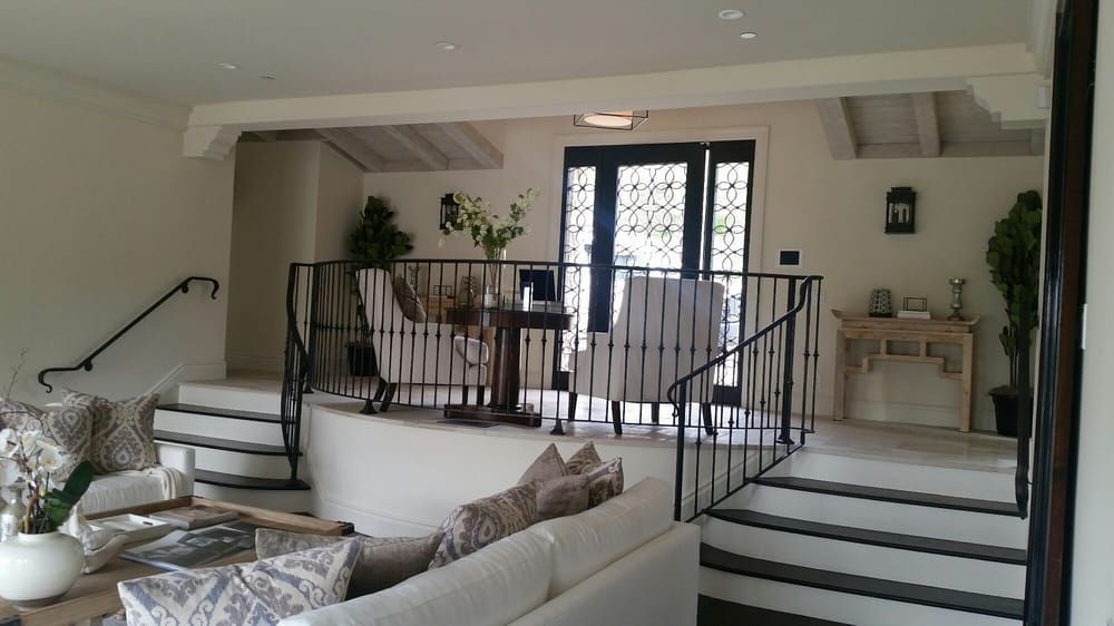 Bright living room with white walls, black railings, steps, sofa, plants, and double glass doors