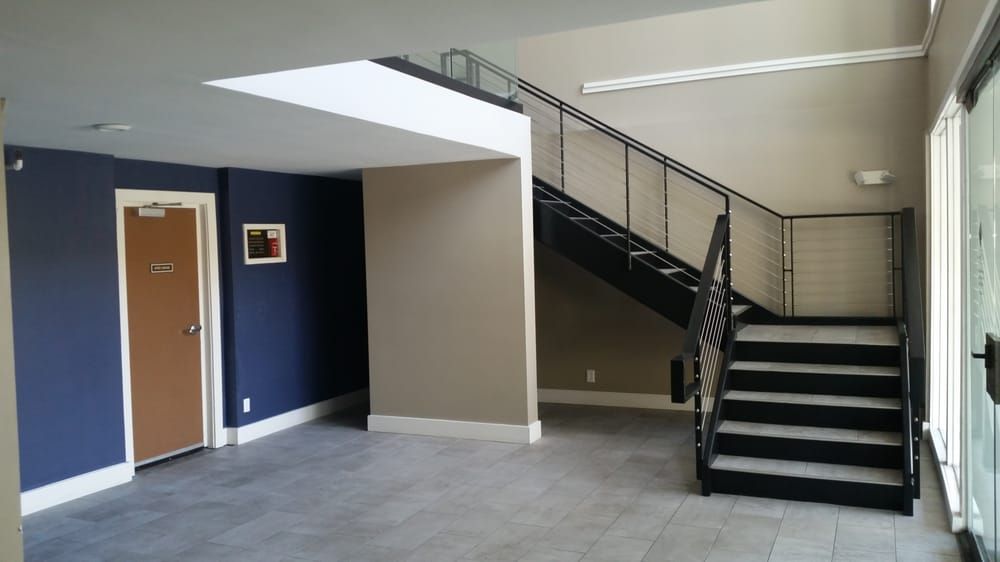 Empty indoor lobby with blue accent wall, door, and staircase with black railings