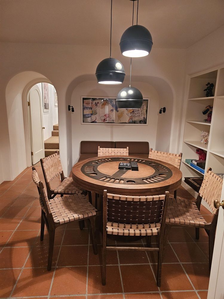 Dining room with round wooden table, woven chairs, terracotta floor, and three black pendant lights.