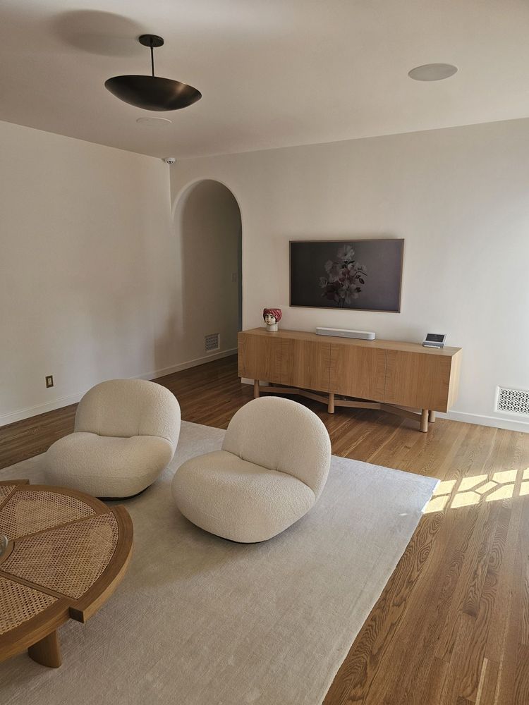 Minimalist living room with beige lounge chairs, wood floor, arched doorway, and console beneath wall art.