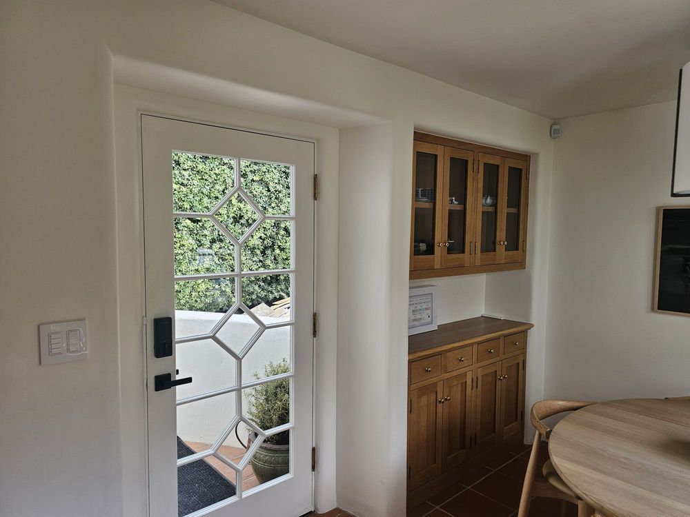 Bright kitchen with glass-paneled door, wooden cabinets, and a round table near the window.