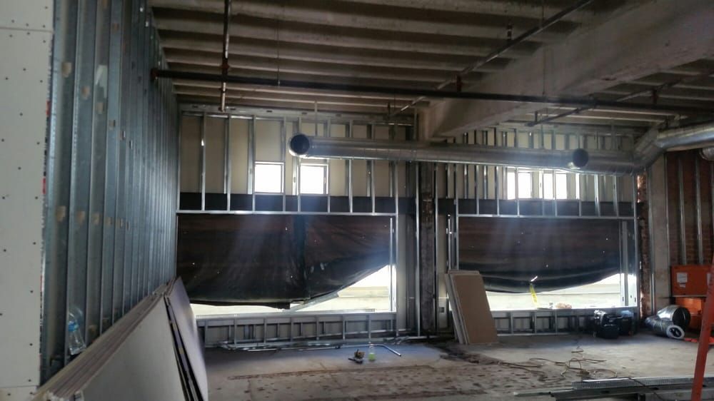 Interior of a metal warehouse under construction, with large dark panels and scattered materials on the floor