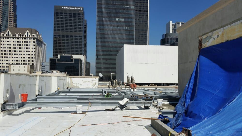 Rooftop construction area with white roofing, blue tarp, and city skyscrapers in the background