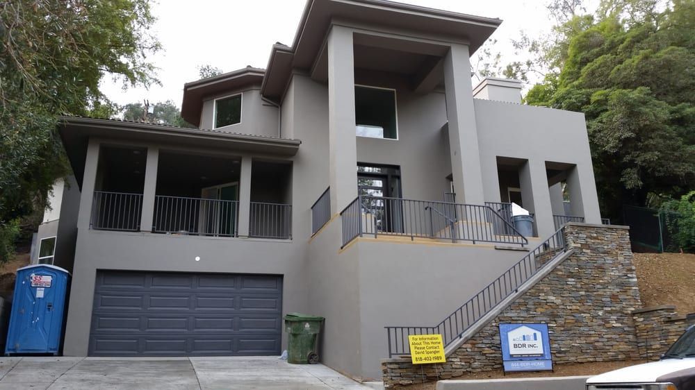 Gray hillside house with garage, stone retaining wall, and front stairs with railings