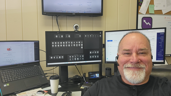 Jeffrey Fagan at desk with triple monitors and video-call setup in an office workspace