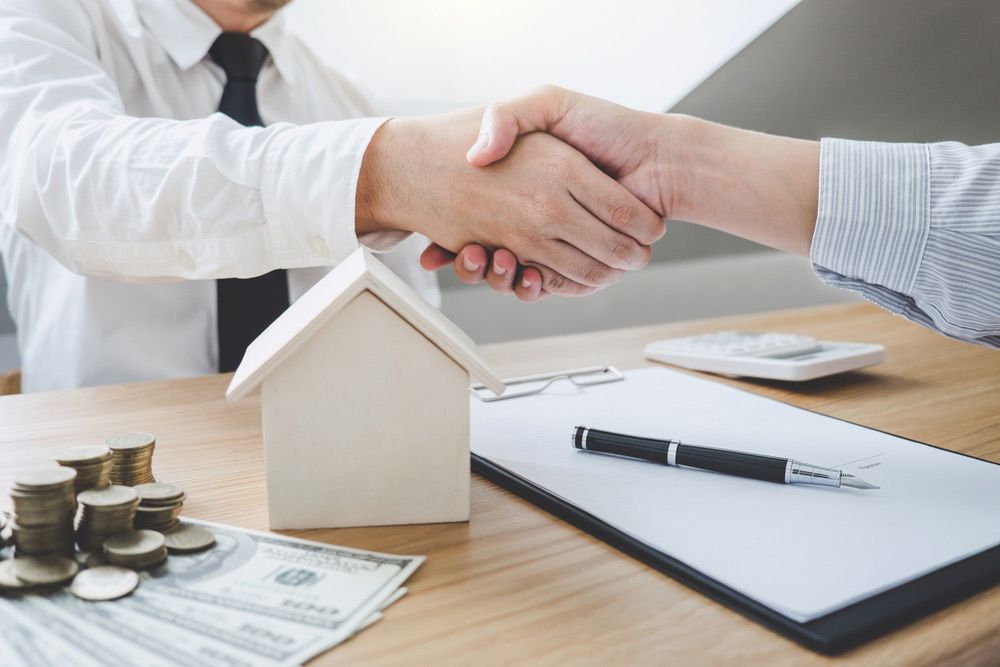 A Man is Shaking Hands With Another Man in Front of a Model House — Cairns Property Collective in Kanimbla, QLD