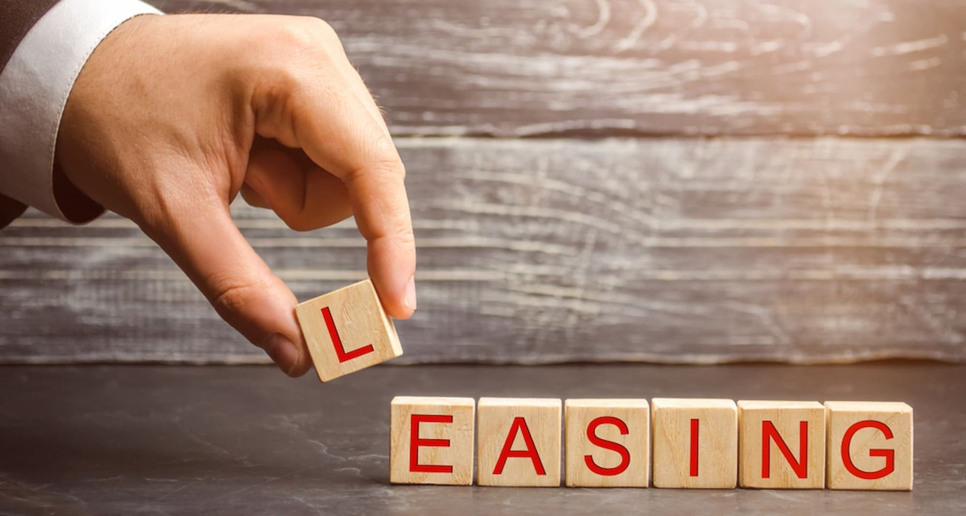 A Hand Is Holding a Wooden Block with The Word Leasing Written on It — Cairns Property Collective in Trinity Park, QLD