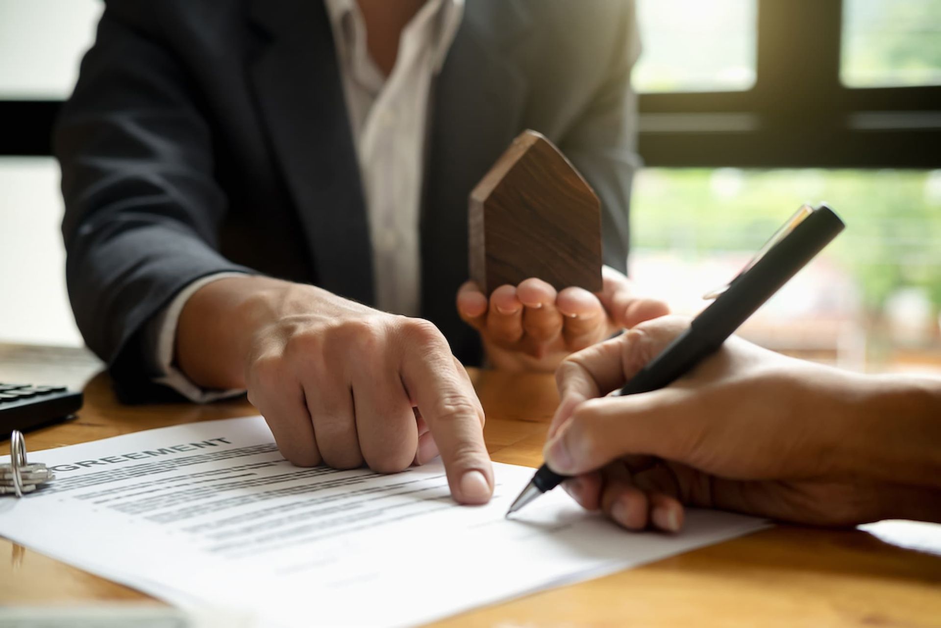 A Man Is Holding a Model House While Another Person Signs a Document — Cairns Property Collective in Edmonton, QLD