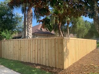 A wooden fence is surrounded by trees and grass in front of a house.