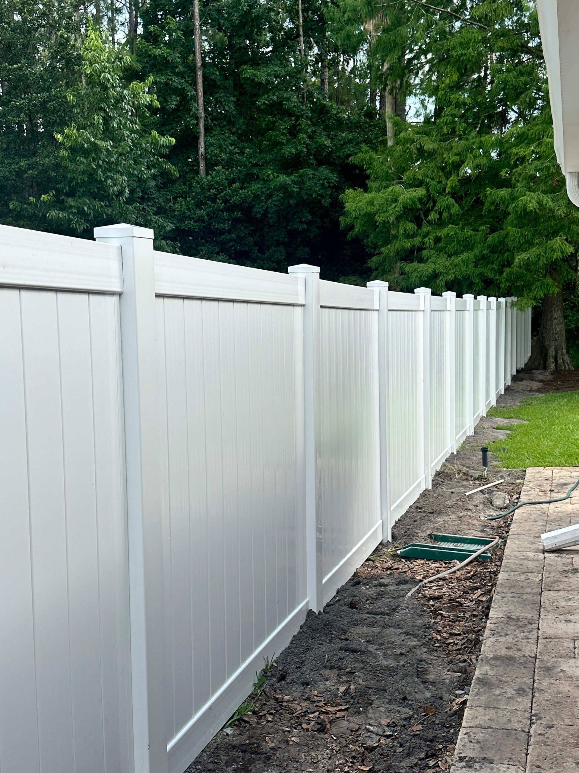 White vinyl privacy fence along a grassy yard beside a house under a cloudy sky