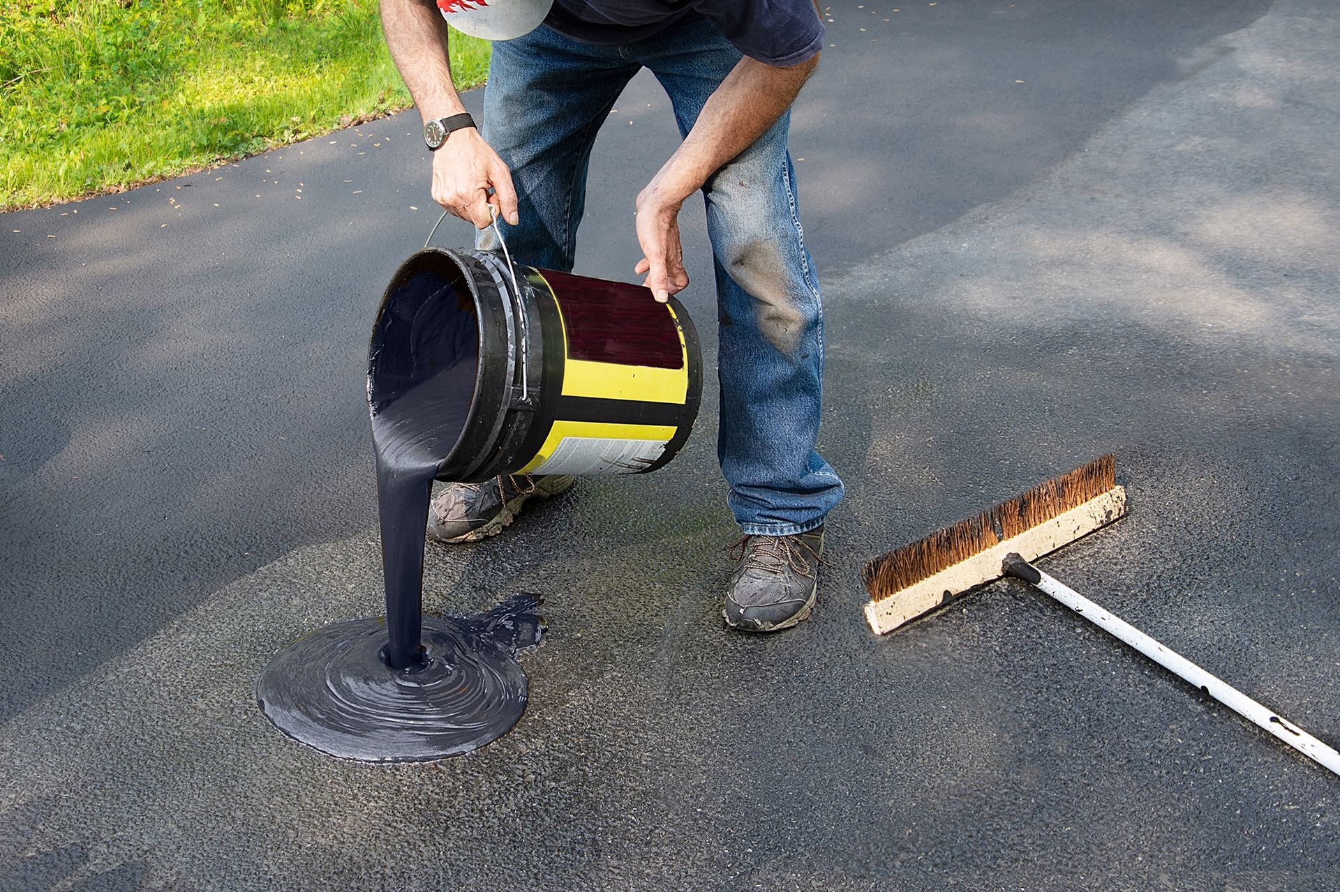 A man is pouring asphalt from a bucket onto a road.