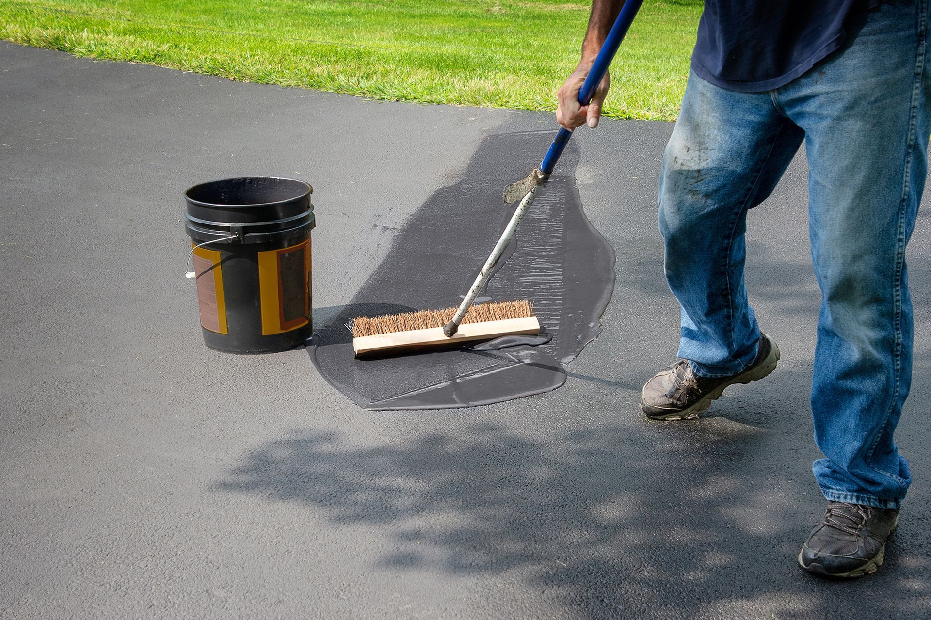 A man is applying asphalt to a driveway with a broom.