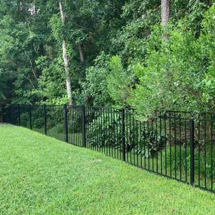 Black metal fence along a grassy slope with dense green trees in the background