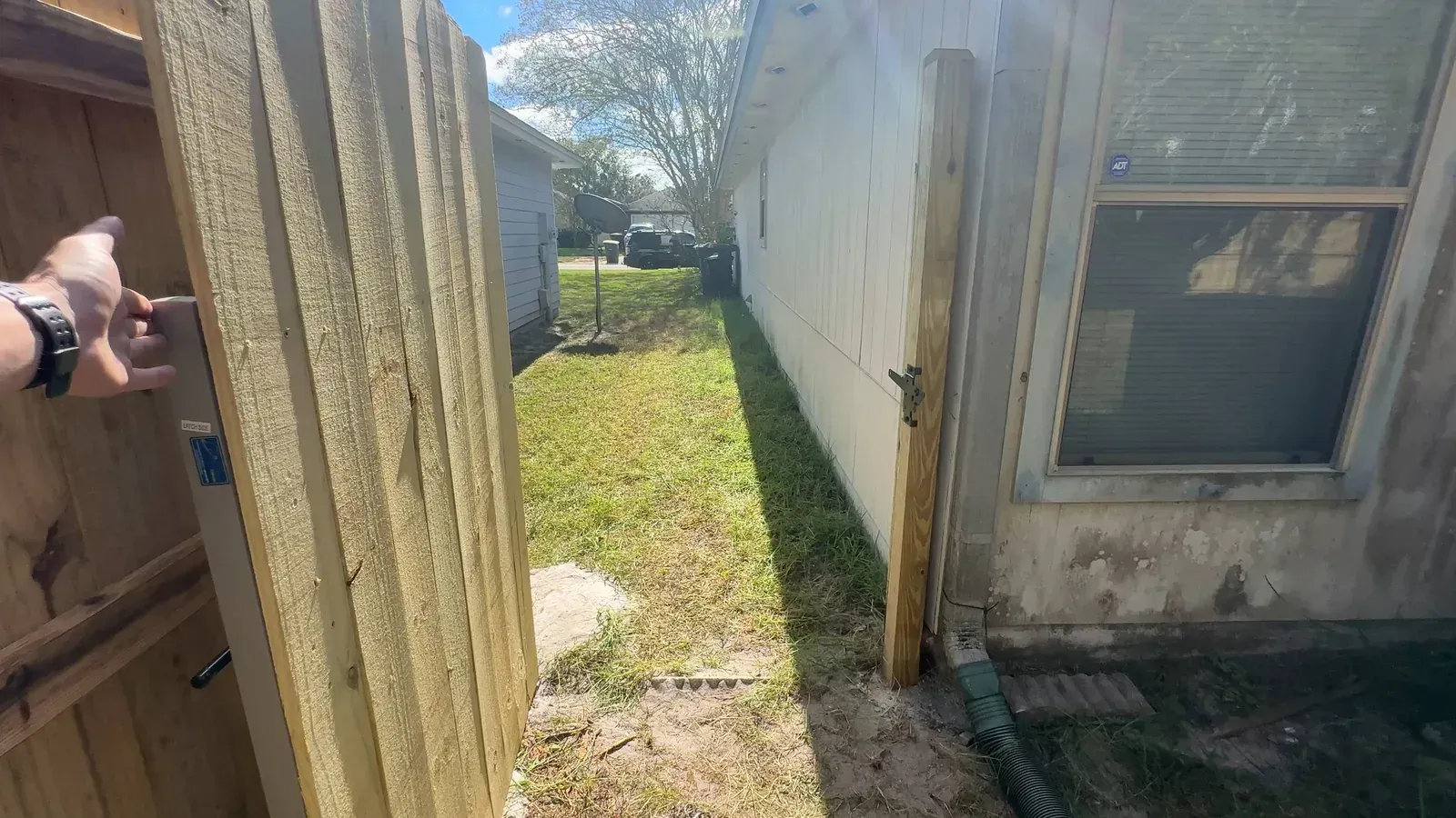 Wood fence panel being set in place beside a house wall during installation