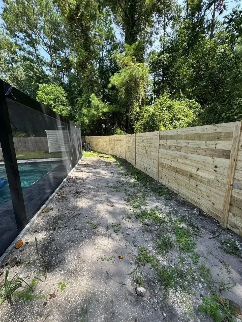 Wood fence beside a walkway and screened pool enclosure
