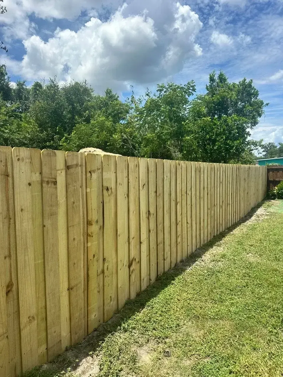 Straight run of new wood privacy fence across an open grass backyard