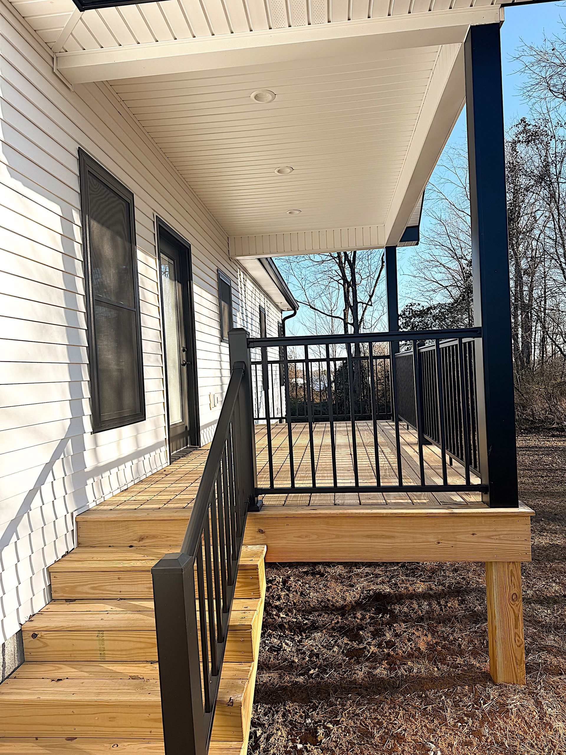 A wooden porch with steps leading to a house with black railings and columns.