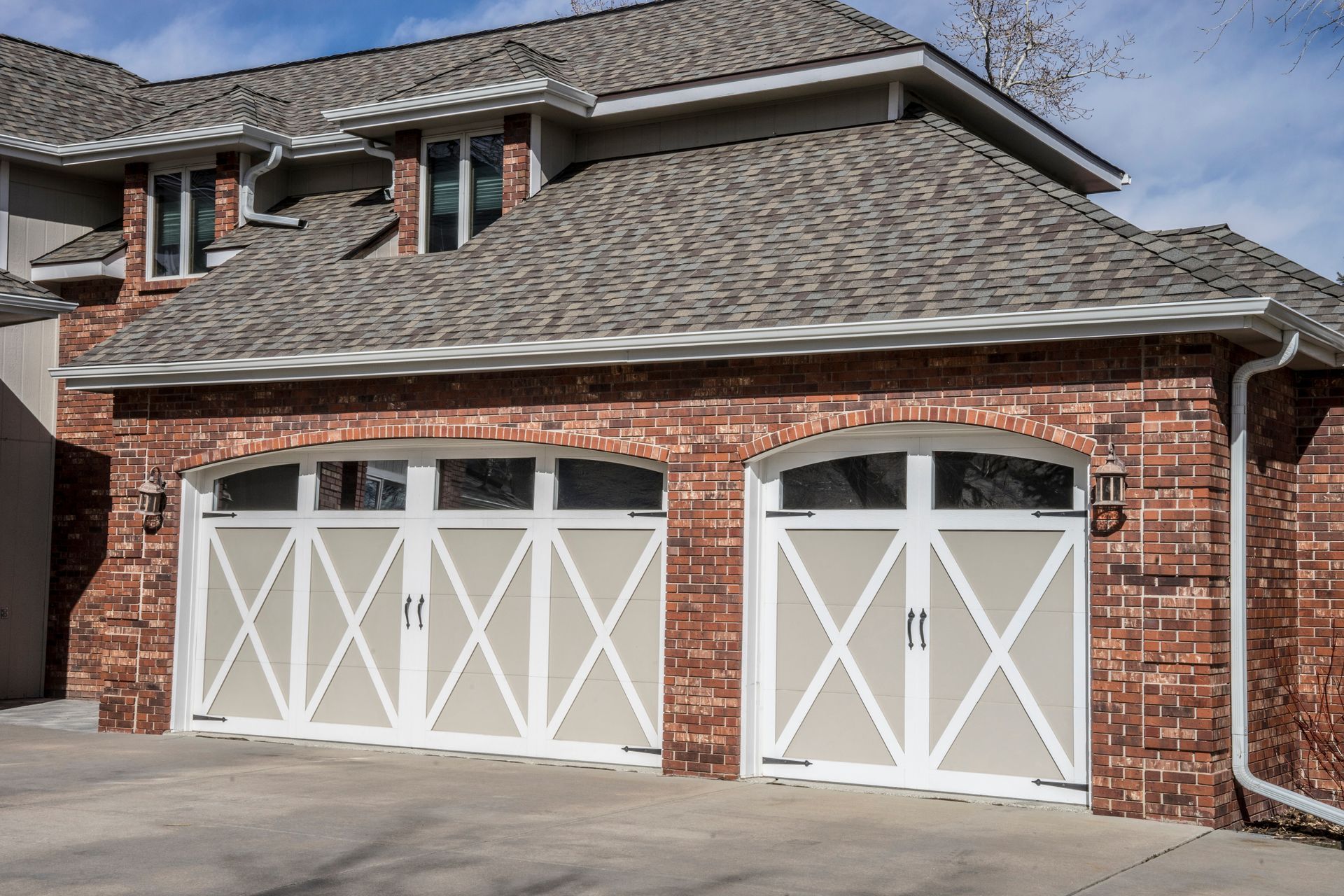 A carriage-style garage door in white and beige hues on a home with a brick exterior