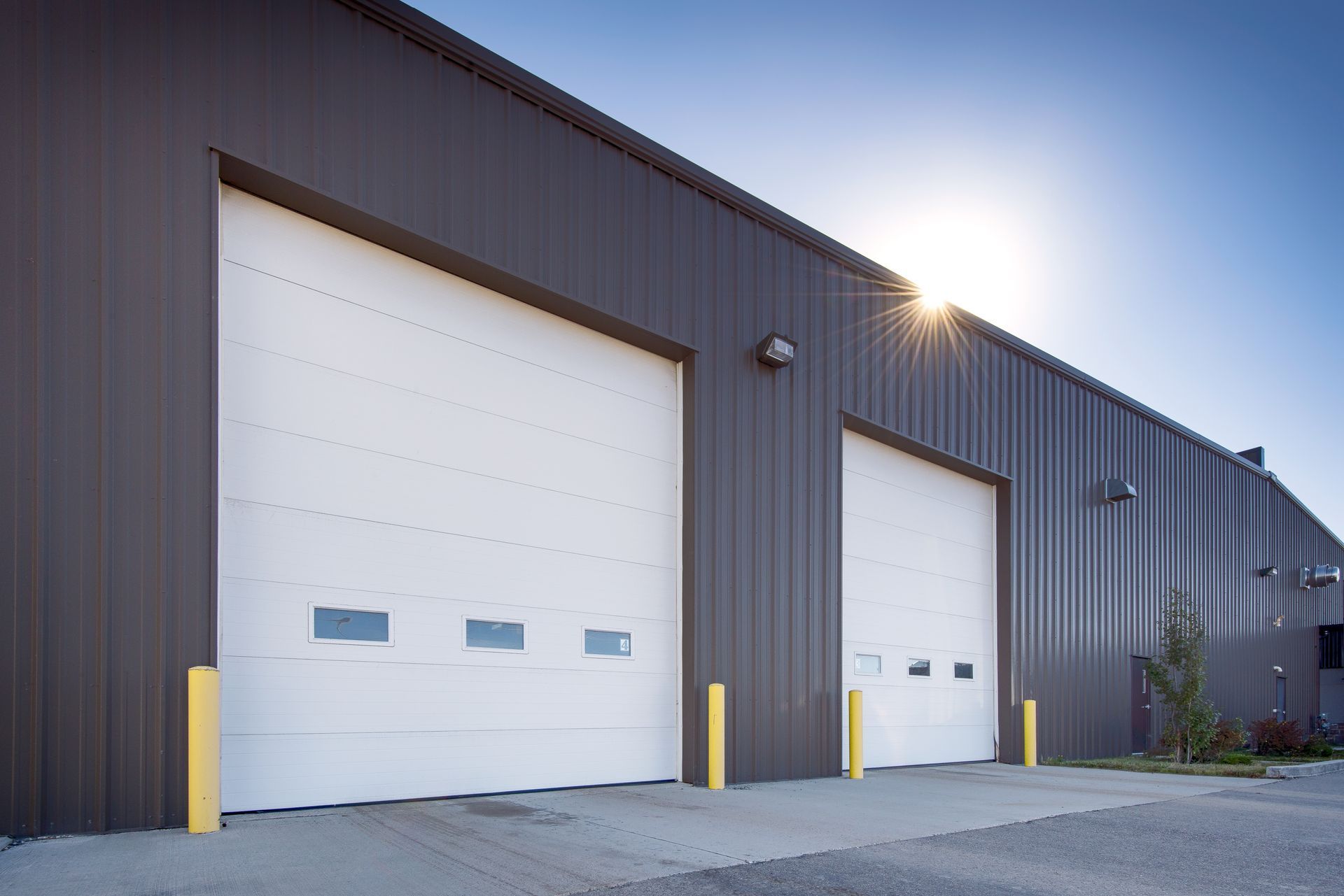 An exterior shot of two sets of white commercial garage doors with small windows