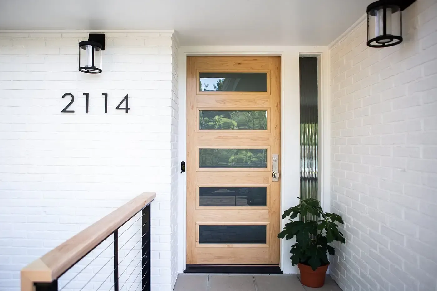 White house entrance with black trim, stone, and bushes.