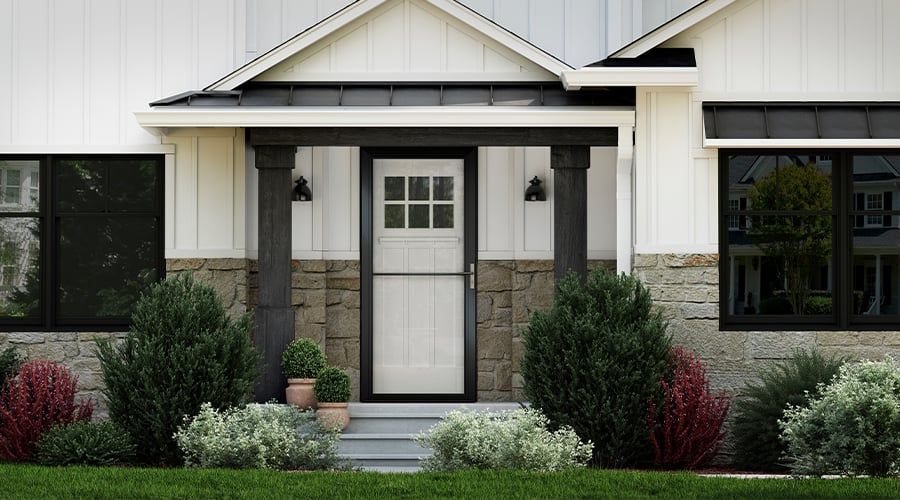 White house entrance with black trim, stone, and bushes.