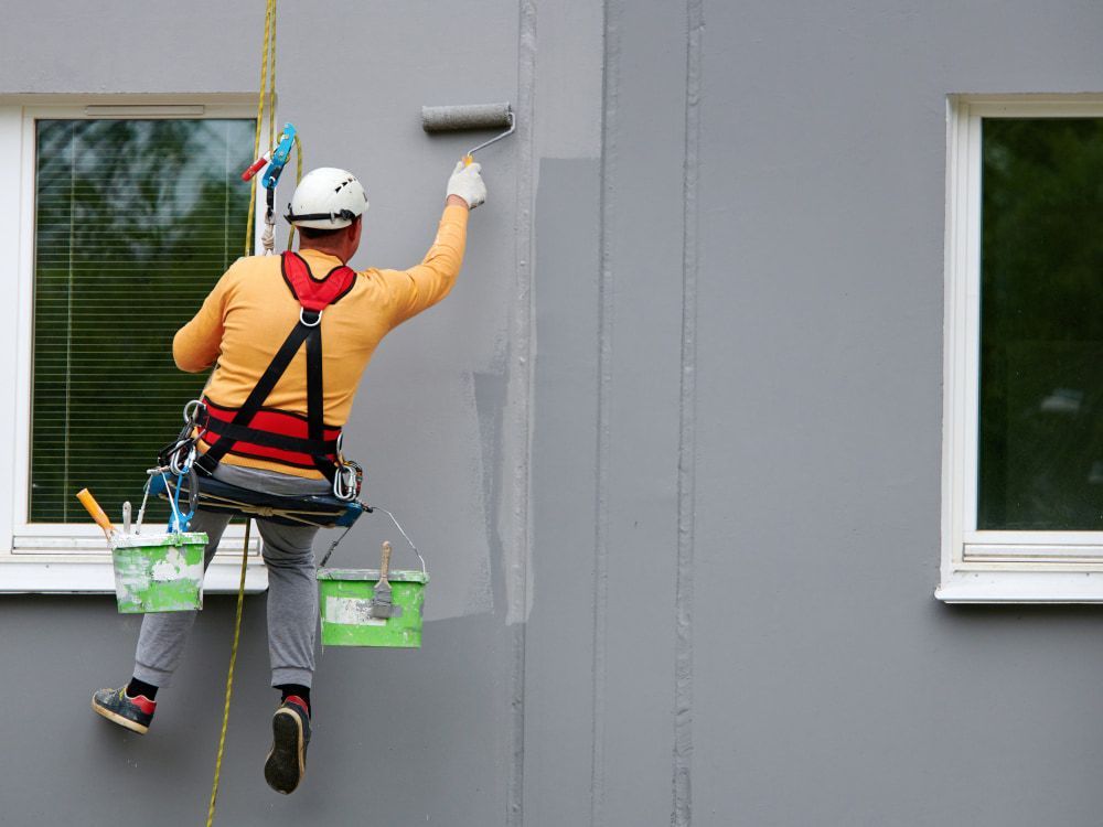 Man Painting a Gray Wall While Suspended by Ropes — BK Painting & Property Maintenance in Gladstone, QLD