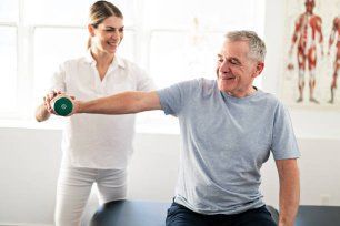 A Woman Is Helping an Older Man Lift a Dumbbell — Illawarra Sports Injury Rehabilitation and Physiotherapy Centre in Bellambi, NSW