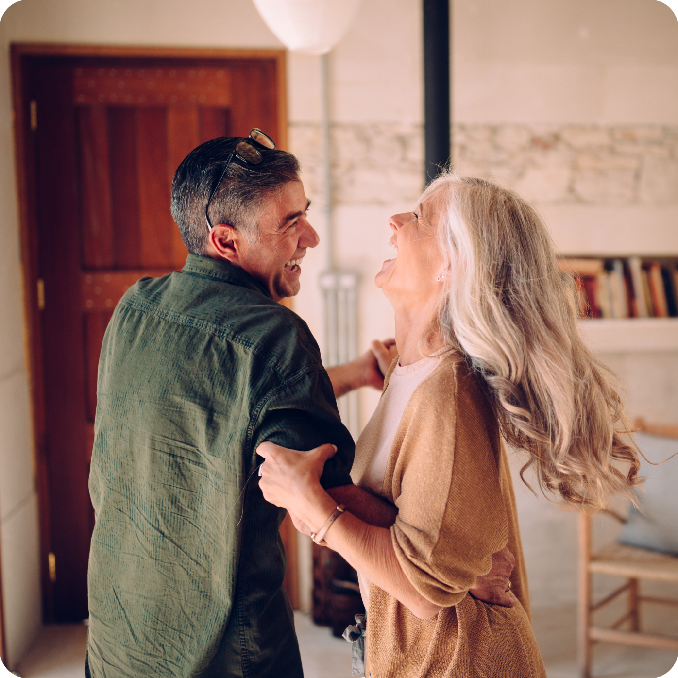 Two people smiling and dancing together in a cozy room with a wooden door and bookshelf.