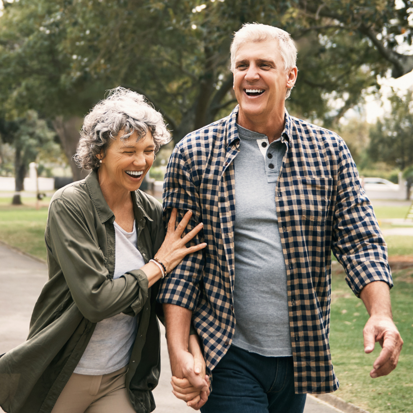 Two smiling people walking in a park, one in a plaid shirt and one in a green cardigan