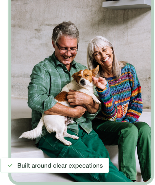 Smiling couple in colorful clothes holding a small dog on a bench indoors