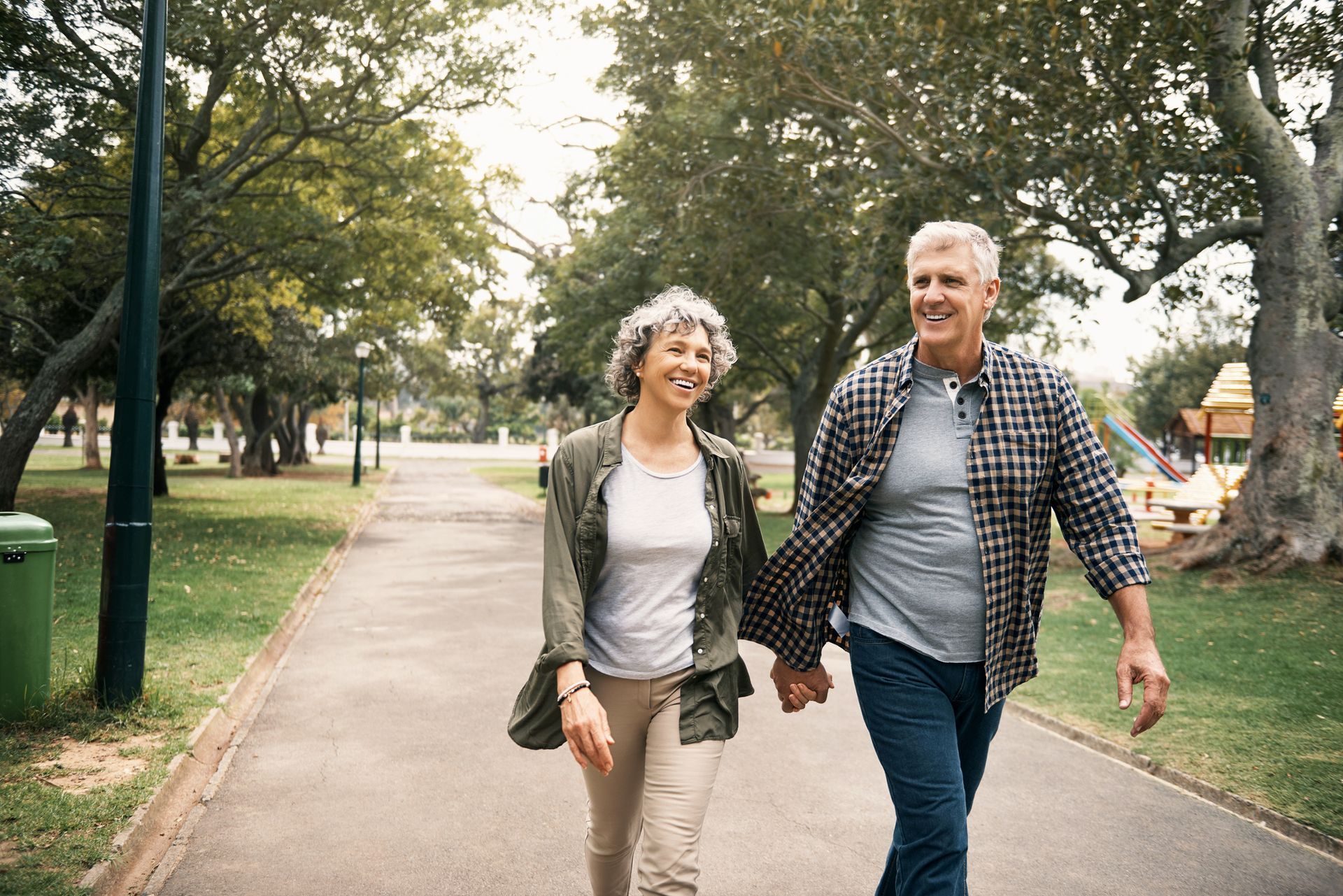 Two people walking hand in hand on a tree-lined park path, smiling.